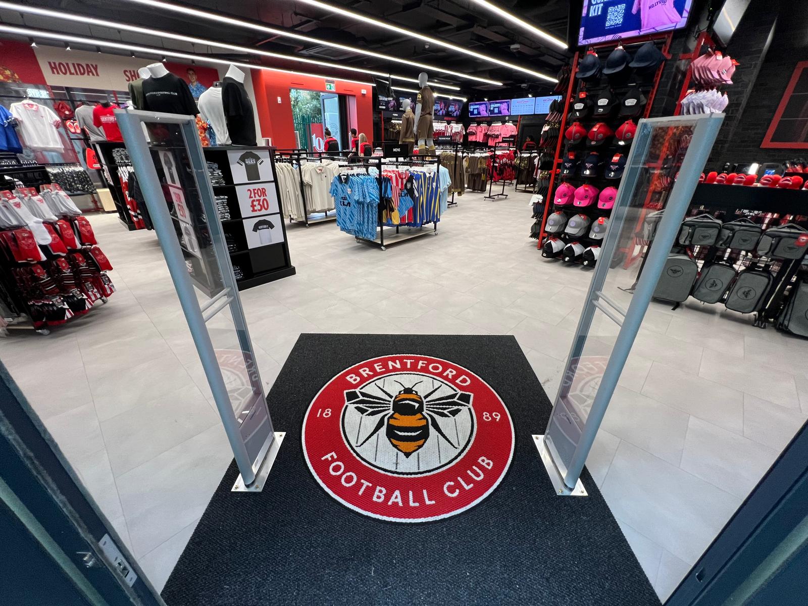 Entrance to Brentford FC Fanstore showing a grey precision nib logo mat with the Brentford FC Emblem designed and made by COBA Flooring.