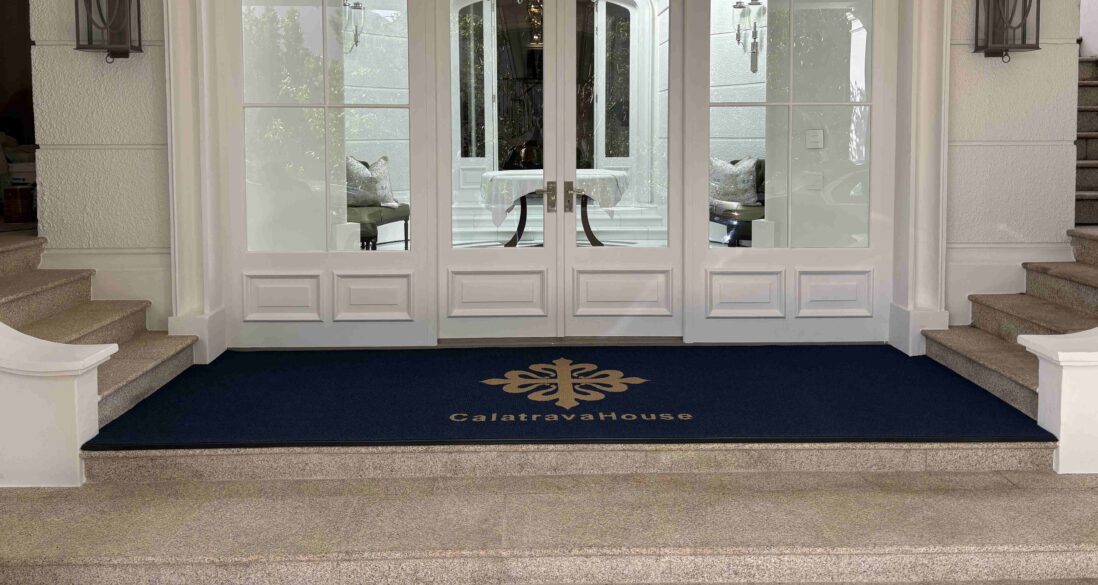 Custom Logo Mats at the entrance of Calatrava House with a navy mat and gold branding in front of elegant glass doors.