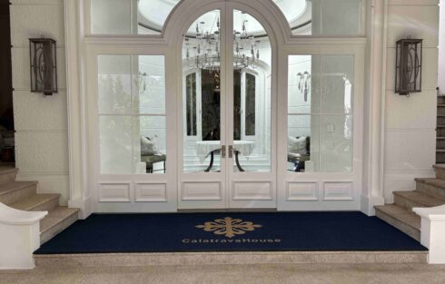 Custom Logo Mats at the entrance of Calatrava House with a navy mat and gold branding in front of elegant glass doors.