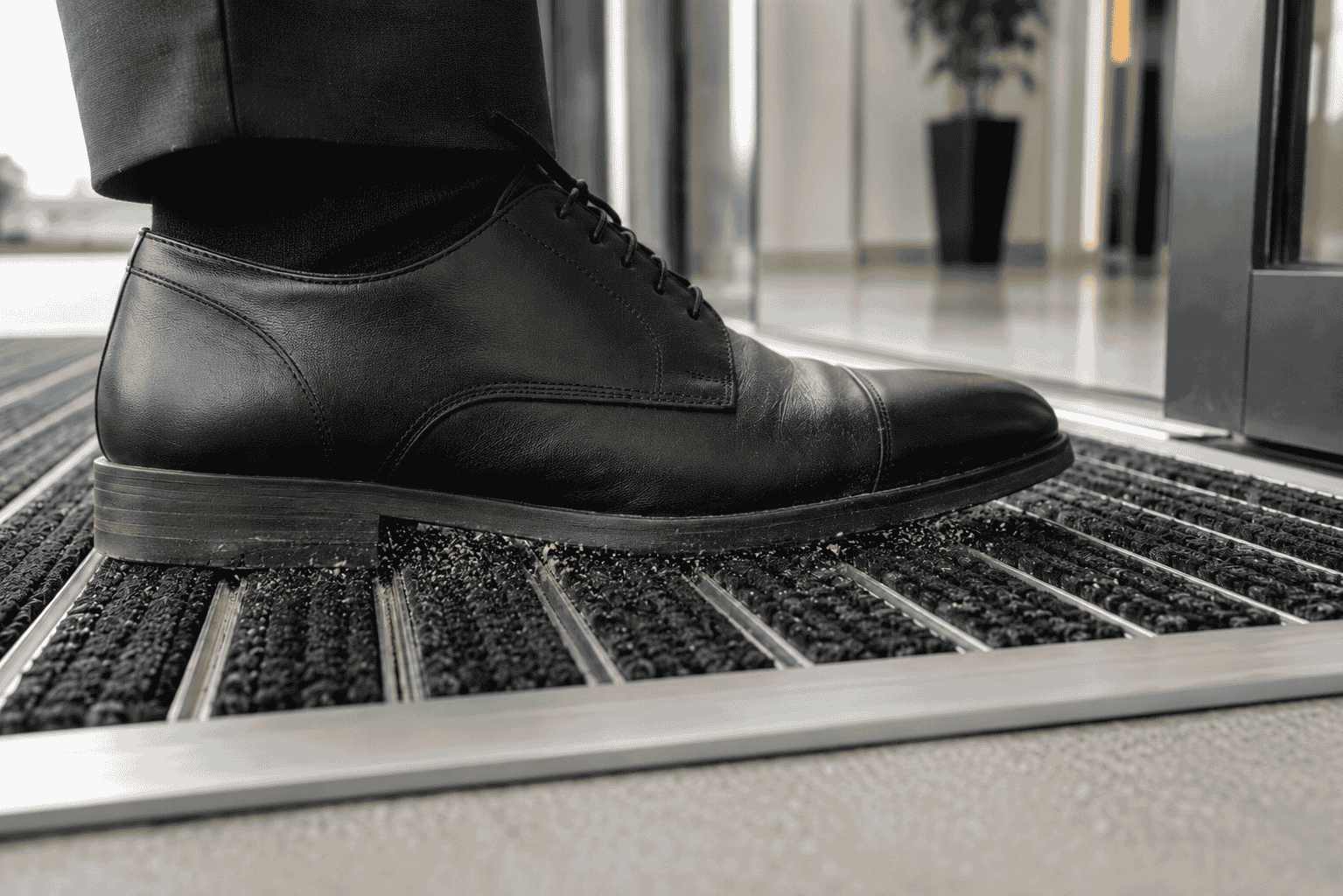 Close-up of a black shoe stepping onto a commercial entrance mat as dust and grit are scraped from the sole.